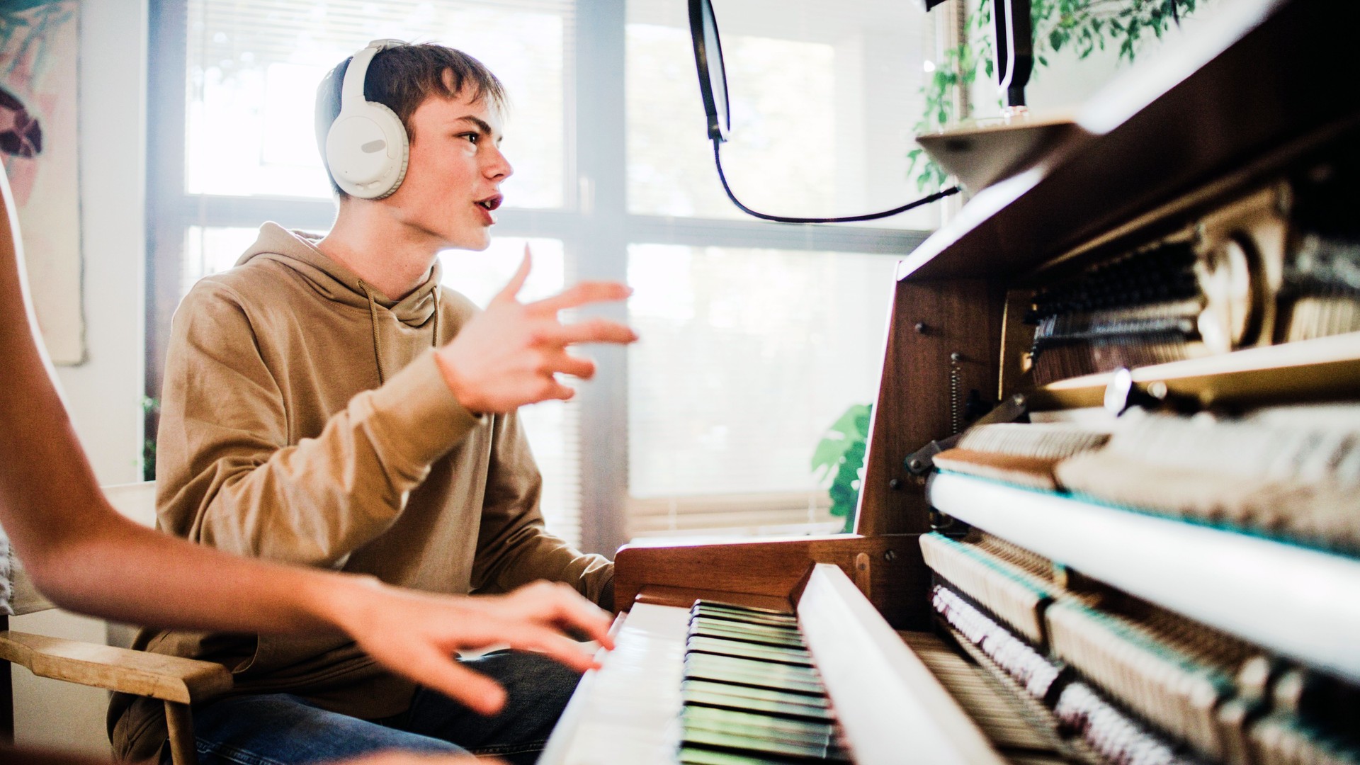 Male student wearing headphones practicing singing lessons and female player playing background music on the piano